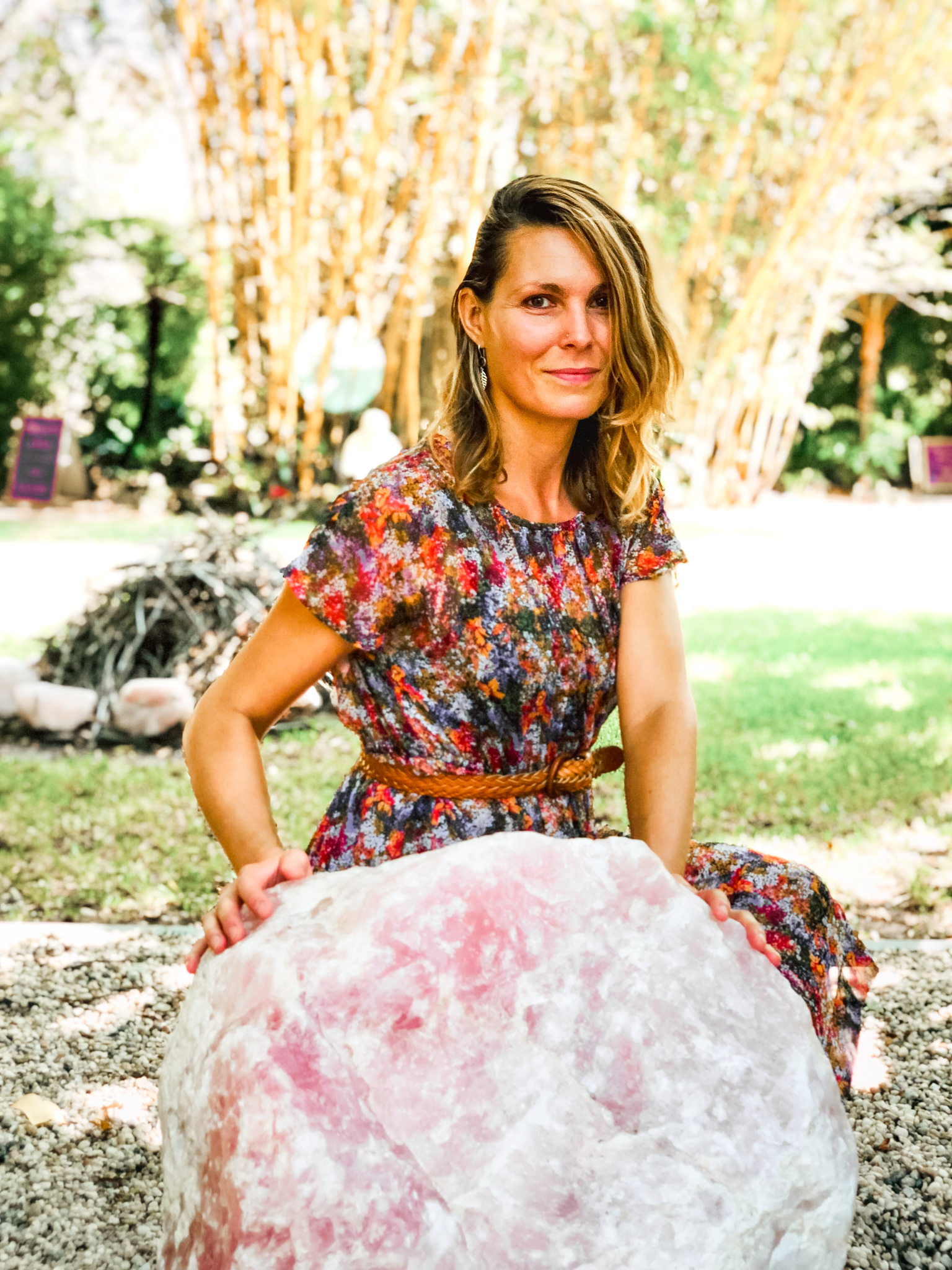 blond woman sitting in front of a big rose quartz crystal